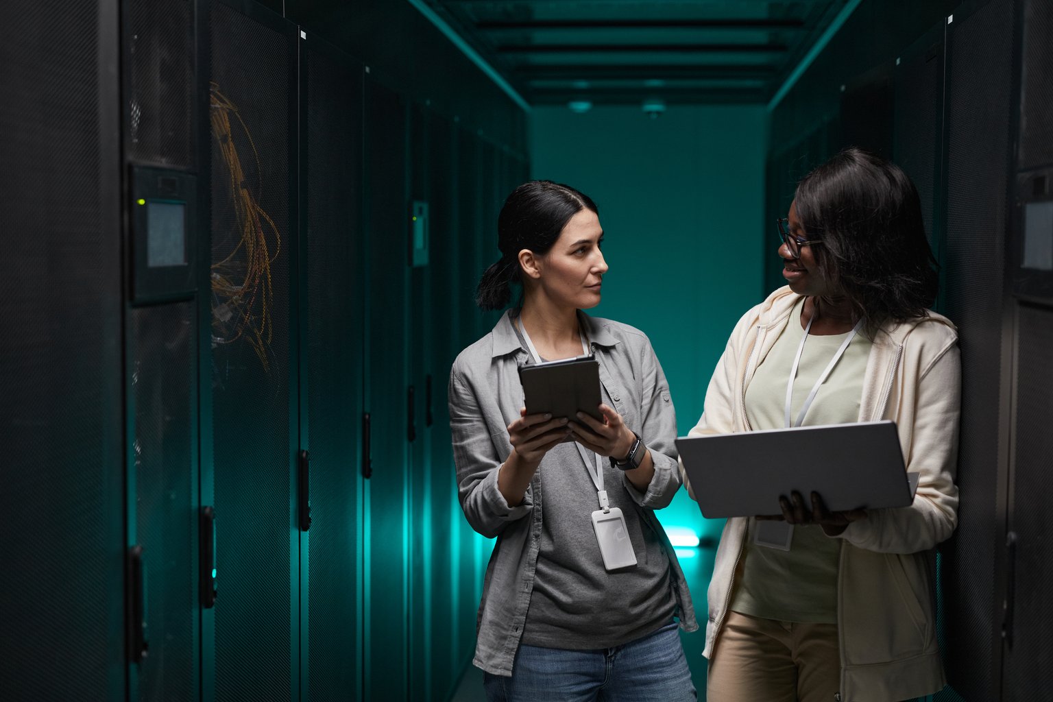 Two staff members reviewing data on a tablet and laptop in a server room